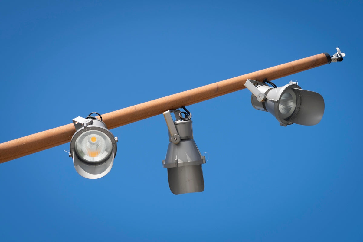 Three spotlights on a pole with a blue sky in the background