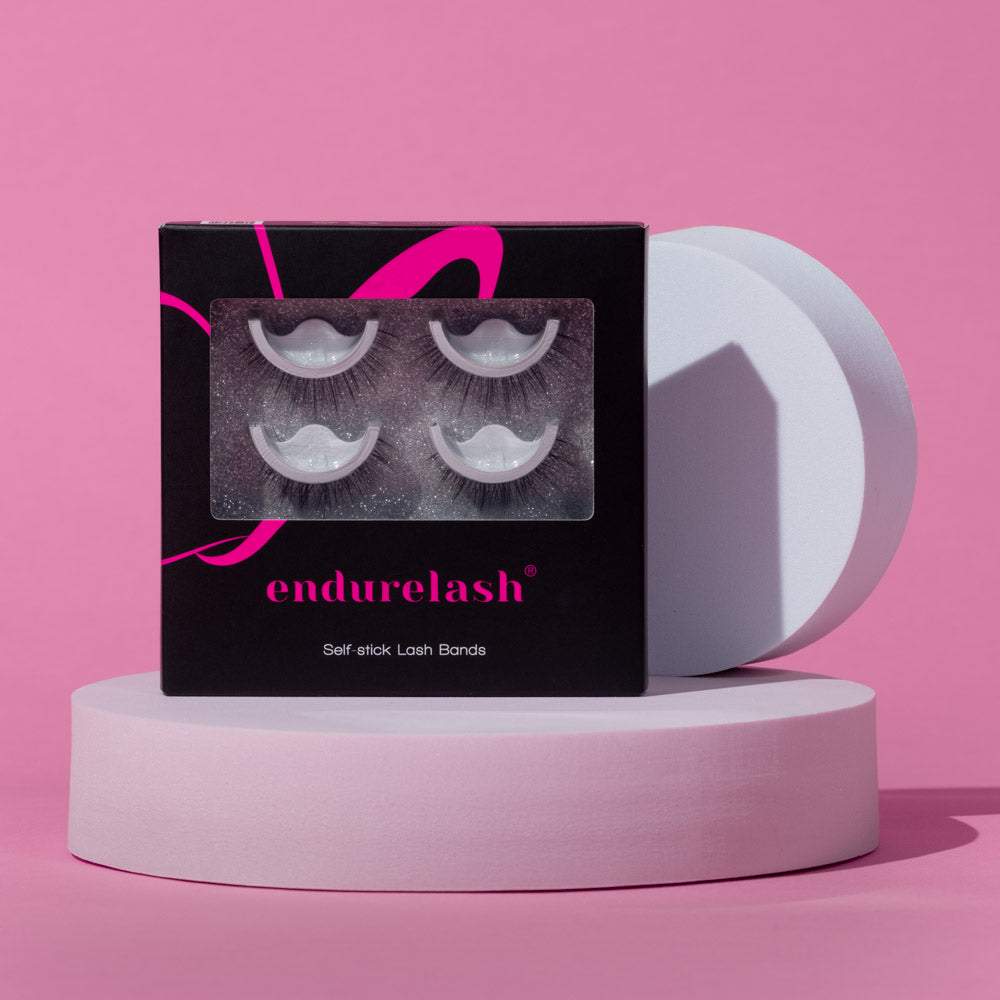 A box of EndureLash self-stick lash bands, displayed on a pink two-tone stand with the front of the box, its product, product name, and brand visible.