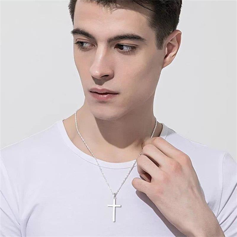 Man wearing a white shirt and a silver cross necklace against a plain background. Christian cross jewelry.