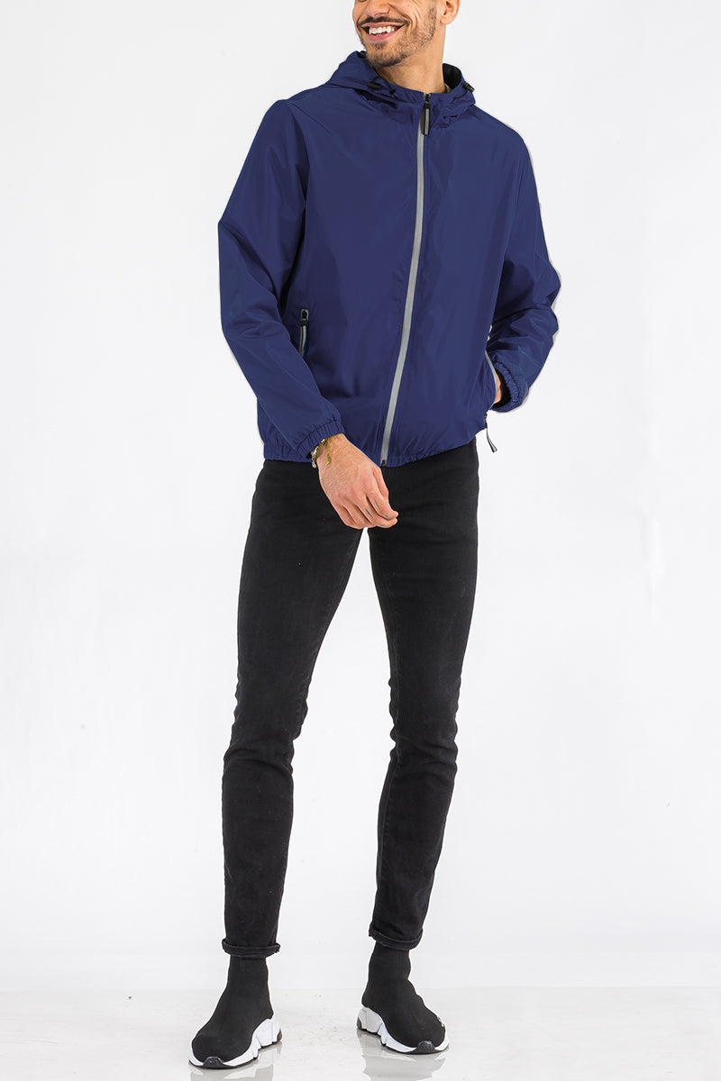A full body view of a male model wearing the reflective navy blue zip up wind breaker jacket.