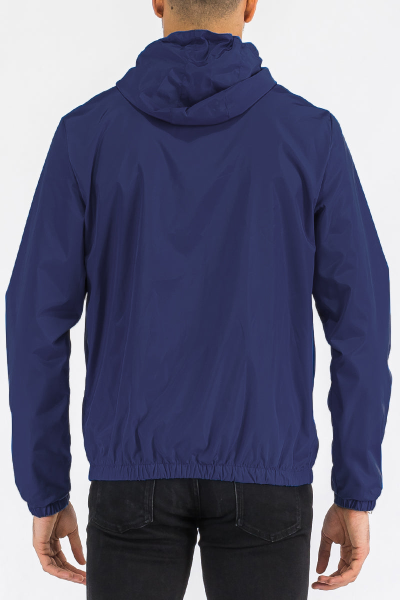 A rear view of a male model wearing the reflective navy blue zip up wind breaker jacket.