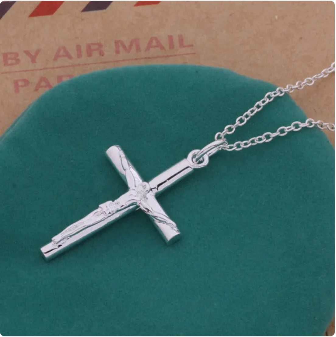 Silver cross pendant necklace on a green surface.