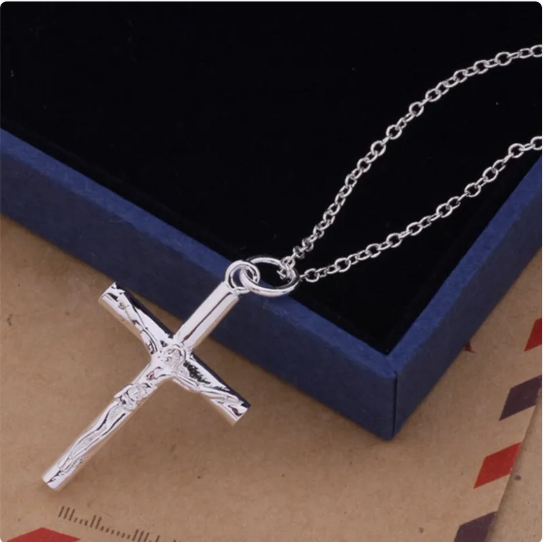 Silver crucifix pendant on a chain against a jewelry box.