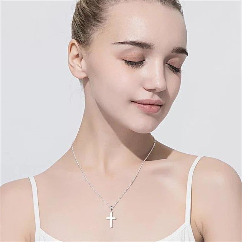 Woman wearing a silver necklace with a cross pendant on a plain background. s925 Christian jewelry.